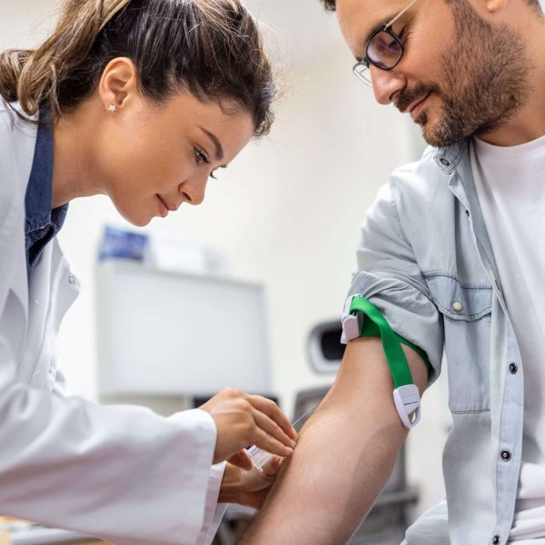 Friendly hospital phlebotomist collecting blood sample from patient in lab. Preparation for blood test by female doctor medical uniform on the table in white bright room